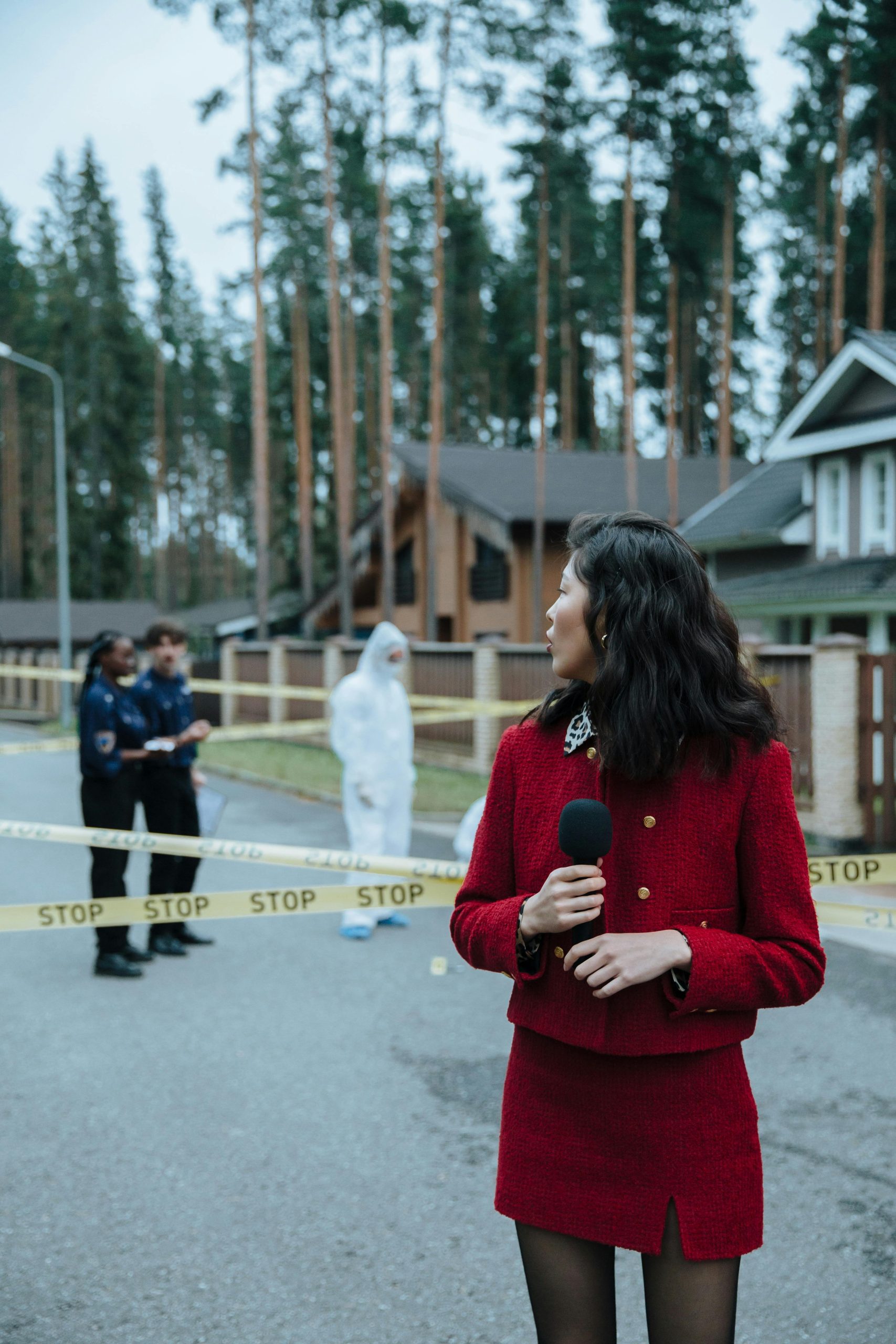 Reporter at a crime scene with police officers and caution tape in a residential area.