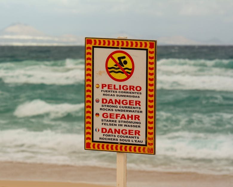A beach warning sign cautioning about strong underwater currents in multiple languages.